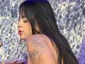 Karina Mendez, com seus longos cabelos pretos, piercing no nariz e tatuagem no ombro direito, seus lábios rosados levemente entreabertos, exibindo sua parte superior do corpo e a colorida arte nas unhas..