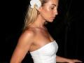 ViktoriiaLu with blonde hair, white flower in her hair, wearing a strapless white dress, showing her tits, earrings, and a focused expression, in a dark background.