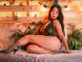 HelenHard with long dark hair, green lace bodysuit, and black strappy heels, sitting on a bed, showing her ass and tits, wearing a green leaf headband.