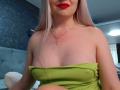 CoquineElise with pale skin, red lipstick, and long blonde hair, wearing a green strapless top, showing her small tits and a gold cross necklace.