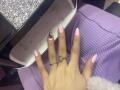 EliseMonet's hand with pink nail polish, ring with gemstone, and pink ribbed sweater, resting on a textured white surface. Her finger's pinkie has a red gem.