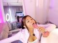 AlessiaFerry with her tongue out, sucking a pink dildo, wearing a white jacket, reflected in a mirror, showing her tits and ass, in a brightly lit room.