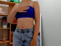 Steisii with a blue strapless top, covering her tits with one hand, wearing high-waisted, slightly distressed denim jeans, showing a flat, tan-lined stomach.
