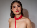 LuciaVargass with red lace halter top, no bra, exposing her tits, has red lipstick, brown hair, and warm brown eyes, standing against a plain background.