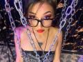 LunaixMoon with glasses, red lipstick, and a black strapless top, has chains in front, and a tattoo on her chest, looking up with a seductive smile.