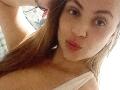 KimFire's selfie shows her pouting with slightly parted lips, blue eyes, and long brown hair. She's wearing a white tank top, showing her small tits. She's raising her arm.