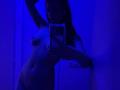 Molray, naked, blue-lit, holding phone in front of mirror, showing small tits and slim ass, arm raised, long dark hair, reflecting in phone screen.