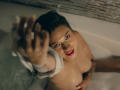 LindaJimenex in a bathtub, nude, with wet skin and dark hair, raising a bound hand, looking up with red lipstick, showing her tits, tattoos on her arm, water in background.