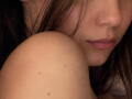 EmeraldCrivaro's shoulder with small moles, brown hair, and pink lips, partially visible. Her nose is centered, and her lips are slightly parted. The image is a close-up shot.