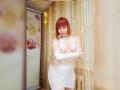 LaylaHottyX with red bob has small tits, wearing a white lace dress, arms crossed, standing in a room with fairy lights and a glass shower.