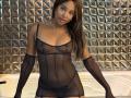 EmmaLatin in sheer black lingerie, showing her tits through the fabric, with long brown hair, wearing black gloves, and a pearl necklace, standing in a white tub.