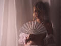 RosaVance with blonde hair in a messy updo, holding a lace fan, wearing a sheer pink top, exposing her small tits, and a pearl necklace, in dim lighting.