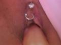 FrenchShanna's pussy with two silver piercings, a heart-shaped one above and a ring-shaped one below, being penetrated by a pinkish, circumcised, erect penis.