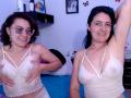 LunaVenus has curly brown hair, glasses, and is covering her small white lace bra-covered tits with her hands. LunaVenus with black hair is raising her arm, smiling.