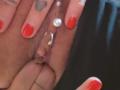 FrenchShanna's hand with red nail polish, holding her pierced pussy, showing a heart tattoo on her index finger, and a pearl ring on her clitoral hood.