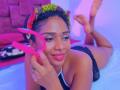 MeganWlliams with dark skin, curly hair, wearing a colorful headband, black lingerie, holding pink hoop earrings, smiling, laying on bed, legs up, ring on finger, nose ring.