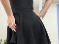 Rorria's hands are on her black, textured skirt. Her skirt is flared and she's wearing a black top. Her skin is light and her fingers are slightly curled.