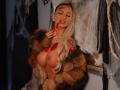 CelineDian with large tits, blood on face, wearing a fur coat, long blonde hair, pearl necklace, touching mouth, tattoo on arm, in a spooky, dark setting.