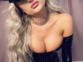 MademoiselleBella with big tits, wearing black latex gloves, a shiny black strapless top, and a diamond necklace, has long wavy blonde hair and pink lips.