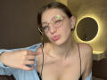 StaceyAverbach with glasses, winking, wearing a blue shirt off-shoulder, black spaghetti strap top, showing her small tits, holding shirt, ring on finger, pouty pink lips, brown hair.