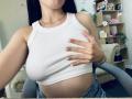 OliviaGranda's white ribbed tank top, showing her big tits, with her hand covering one. She's got black hair, a silver necklace, and denim jeans. Her nail polish is nude.