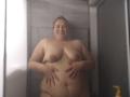 RouseWright is a fat, nude, smiling woman with large, saggy tits and a chubby belly, standing in a shower with hands on her stomach, water droplets visible.