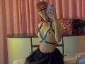 SuriEverly with glasses, pink hair, wearing black leather harness, exposing small tits, and black skirt, taking a mirror selfie in a bedroom.