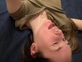 MarishaSchink lying on dark blue bed, head tilted back, tongue out, winking, nose pierced, brown shirt, small heart necklace, brown hair, fair skin, slight blush on cheeks.
