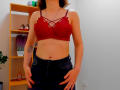 Steisii wearing a red lace bralette, showing her tits, and dark jeans with hands on her hips, has a tattoo on her right arm and brown hair.