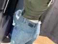 MargoFun's ass in blue jeans with a black button, green shirt, white waistband, and a black belt buckle, standing in a store, wearing a black tag on her shirt.