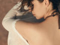 OliviaCluff's bare shoulder and upper back, showing off her white off-shoulder top and brown hair, with a brown choker, in a soft, warm-lighted, close-up shot.