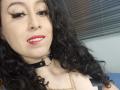 KendraSimons with curly black hair, red lipstick, black eyeliner, wearing a black choker with a metal ring, smiling at the camera, showing her white teeth.