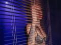 IngaDrein's bare ass and tattooed back are visible through brown blinds, with a blue background and a moonlight reflection. She's wearing a colorful, patterned bikini bottom.