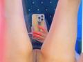 Kkole's legs spread, showing her shaved pussy. She's holding a phone with red nails, taking a mirror selfie. Her phone has a decorative case.