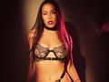 JaneWow with long black hair, red lipstick, black lace bra, black choker, and black straps, showing her tits and a small tattoo on her right wrist.