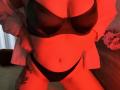 Niferttiti with red-lit skin wearing a black bra and black thong, white shirt open, showing small tattoo on right thigh, hands on hips, medium tits, flat stomach.