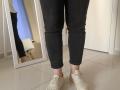 Elliance's ass is in black jeans, and she's wearing beige sneakers with her feet on shiny white tile. A mirror reflects her lower legs.