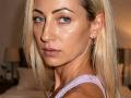 ViktoriiaLu has blonde hair, blue eyes, and a serious expression. She's wearing a pink tank top, with small, visible boobs and a slim, attractive face. Her skin is shiny.