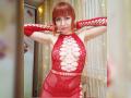 LaylaHottyX with red bob, wearing a red fishnet dress with large cutouts, exposing her tits, standing with arms raised, smiling, in a well-lit room.