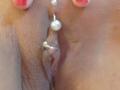 Die französische Shanna hat eine silberne Piercing an ihrem Kitzler, mit zwei kleinen, weißen Kugeln auf beiden Seiten des Piercings. Ihre mit rosa Nagellack versehenen Finger halten sanft ihre Schamlippen..