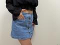 Tilliana's blue denim skirt with brown buttons, black sheer top, and pink nails, showing her hand in the skirt pocket, exposing her bare lower belly.
