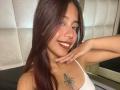 ScarletLuv with dark brown hair, nose ring, and smiling red lips, showing off her tits with a tattoo of a dagger and flower on her left chest.