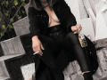 ArianaBlonde with black coat, black leather pants, and exposed tits, sitting on concrete stairs, holding a cigarette and a bottle with a gold cap.