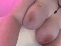 NikkiKisss's big, pale tits with pink nipples and a small heart tattoo near her right areola. She's wearing a necklace with a black and red gem.