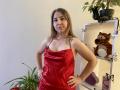 Aminas with medium tits, wearing a shiny red satin dress, hands on hips, standing in front of a shelf with a tiger stuffed toy and butterflies.
