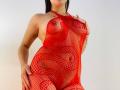 KatarinaNovak wearing a red mesh dress, her tits and pussy clearly visible through the fabric, with one hand on her hip, standing against a plain white background.