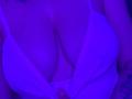 Olieri's big tits in a white, deep-cut top, showing a lot of cleavage, with a purple-blue tint, and a tattoo on the right arm, slightly visible.