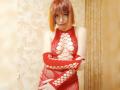 LaylaHottyX with orange bob, wearing red fishnet dress, exposing her tits through large circular cutouts, arms crossed, standing in a warmly lit room, looking at the camera.