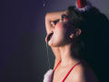 LindaJimenex with tongue out, drooling, wearing red bra and Santa hat, hand behind head, dark background, red eyeliner, white fluffy trim on hat, slightly flushed.