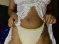 JenifferStar's tan skin, lace top, and white panties with yellow trim, showing a belly button piercing and tattoos on her thighs, holding up her lace top.